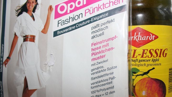 Eine Dame in einem wei&szlig;en Kleid steht neben einer Flasche Apfelessig. Sie zeigt Tipps zum Waschen von Feinstrumpfhosen.