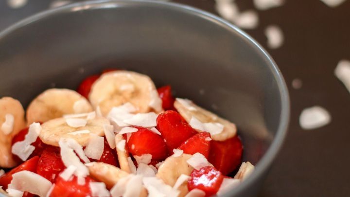 Ein grauer Sch&uuml;ssel enth&auml;lt frisch geschnittene Erdbeeren und Bananen, garniert mit Kokosraspeln.