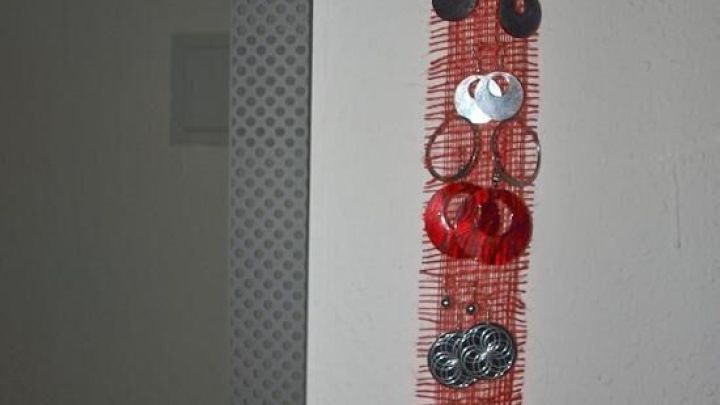 Eine dekorative Ohrringaufbewahrung aus rotem Material h&auml;ngt an der Wand und zeigt verschiedene Ohrringe in bunten Designs.