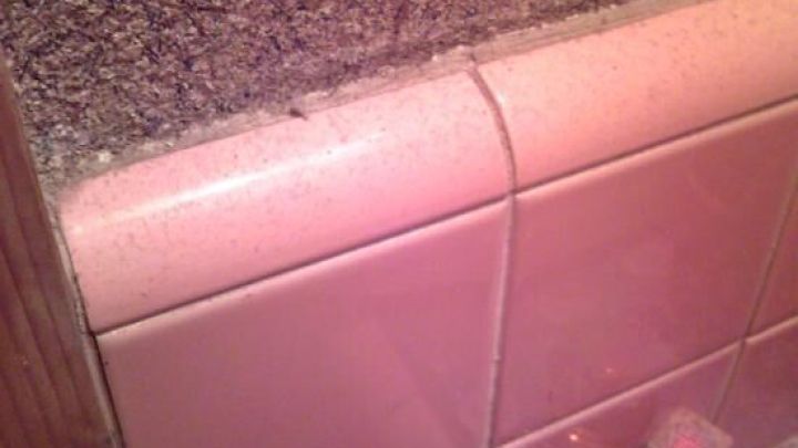 Nagelfeile liegt auf pinken Fliesen in einem Badezimmer neben einer kleinen Parf&uuml;mflasche; rustikale Wand als Hintergrund.