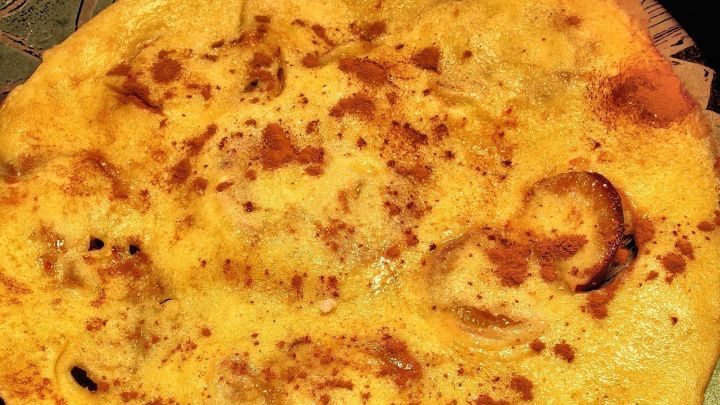 Ein goldgelber Zwetschgenpfannkuchen liegt auf einem Teller, warm und knusprig, bereit zum Genie&szlig;en in einer gem&uuml;tlichen K&uuml;chenszene.