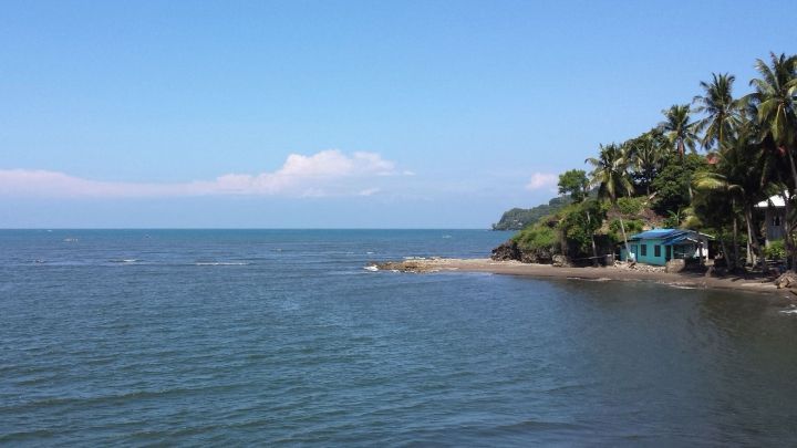 Ein ruhiger Strand mit klarem Wasser, wo Wellen leicht gegen die K&uuml;ste schlagen, umgeben von Palmen und Himmel.