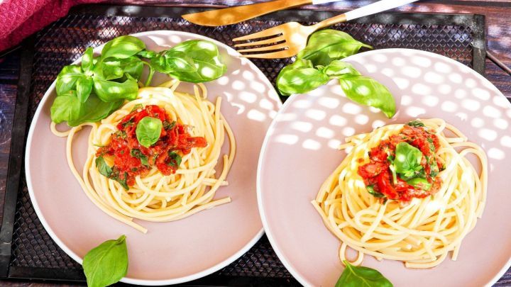 Spaghetti mit Tomatensauce und frischem Basilikum auf Tellern, gem&uuml;tlich serviert auf einem Tisch.