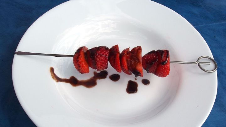 Auf einem wei&szlig;en Teller liegen Obstspie&szlig;e mit Schokolade &uuml;berzogen, umgeben von einer blauen Unterlage.