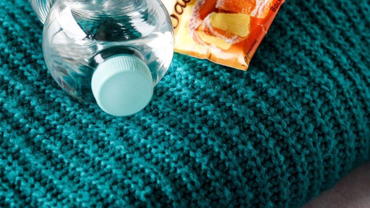 Ein gr&uuml;nes Wollkleidungsst&uuml;ck liegt gestapelt mit einer Flasche Mineralwasser und einem P&auml;ckchen Backpulver daneben.