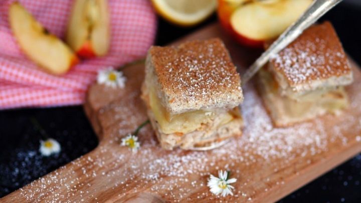 Geraspelte Sommer&auml;pfel liegen auf einem Holzbrett, umgeben von K&auml;sest&uuml;ckchen und frischen Zitronen, leicht mit Puderzucker best&auml;ubt.
