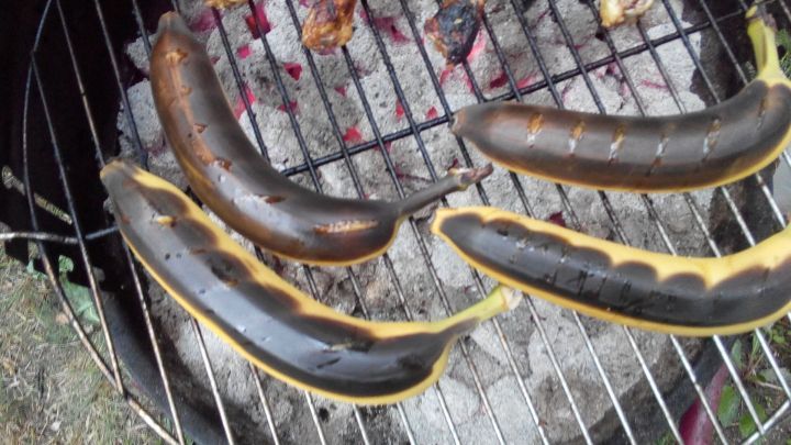 Gegrillte Bananen liegen auf dem Grill, w&auml;hrend sie langsam garen und von der Glut umgeben sind.