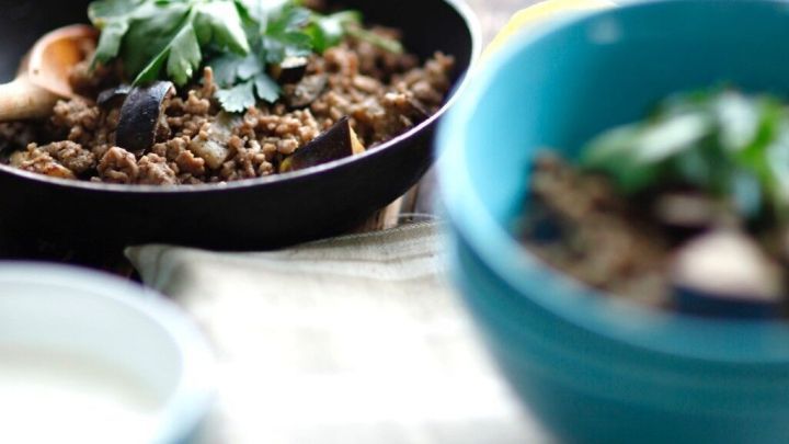 Karniyarik wird in einer Pfanne serviert, w&auml;hrend eine Sch&uuml;ssel mit frischen Zutaten und Joghurt im Hintergrund steht.