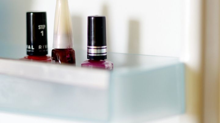 Drei Nagellackflaschen stehen auf einem transparenten Regal, bereit, angewendet zu werden, um Klumpenbildung zu vermeiden.