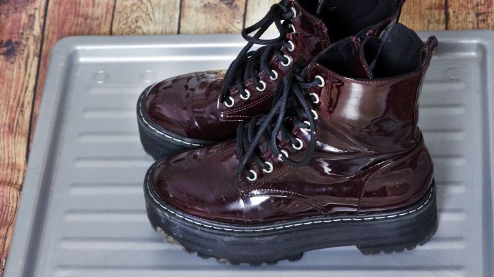 Dunkelrote Stiefel stehen auf einer silbernen Ablage f&uuml;r schmutzige Schuhe, um Schmutz zu sammeln.