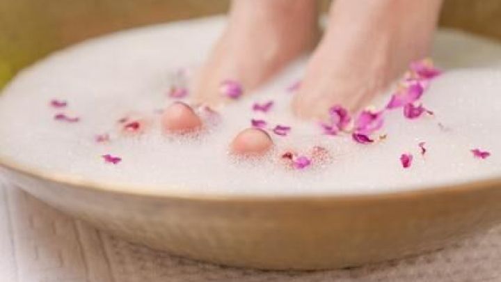 Ein Fu&szlig;bad mit Waschmittel kann gegen Nagelpilz helfen, entspannend und pflegend mit Schaum und Bl&uuml;tenbl&auml;ttern wie auf dem Bild.