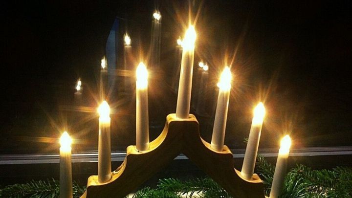 Ein dekorativer Kerzenst&auml;nder mit brennenden Kerzen leuchtet in der Dunkelheit, umgeben von gr&uuml;nen Tannenzweigen f&uuml;r Weihnachten.