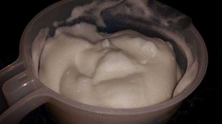 Eine cremige Seifenl&ouml;sung f&uuml;llt einen Messbecher und sch&auml;umt an der Oberfl&auml;che, umgeben von einer dunklen Unterlage.