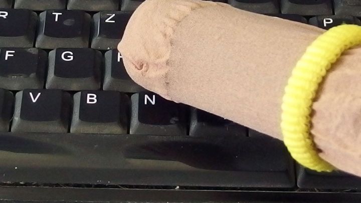Ein Finger in einer Socke tippt auf einer Computertastatur, um die Tastatur schnell zu reinigen.