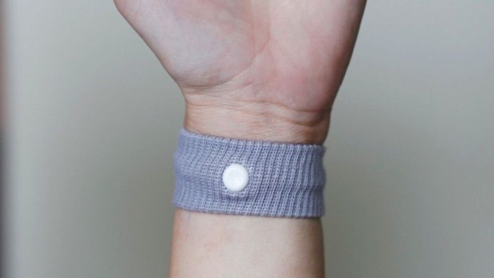 Ein Handgelenk tr&auml;gt ein graues Armband zur Linderung von Reise&uuml;belkeit, w&auml;hrend eine Hand offen pr&auml;sentiert wird.