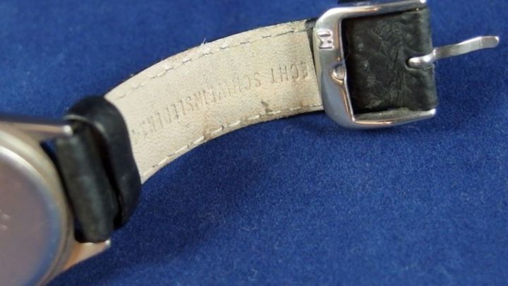 Ein Leder-Uhrenarmband zeigt Abnutzungsspuren durch starken Schwei&szlig;. Es liegt auf einem blauen Hintergrund.