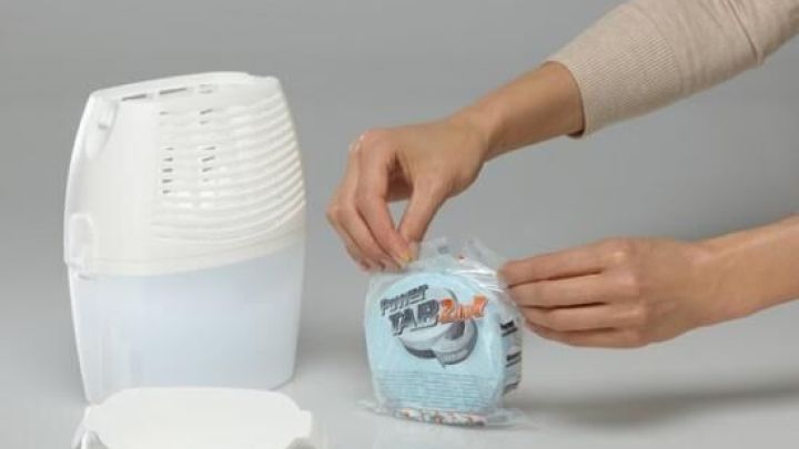 Ein Luft-Entfeuchter steht auf einem Tisch, w&auml;hrend jemand eine neue Technologie-Entfeuchter-Kartusche aus der Verpackung nimmt.