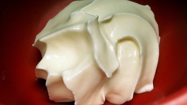 Eine kalorienarme Schlagsahne liegt in einer roten Sch&uuml;ssel und zeigt eine cremige, luftige Textur.