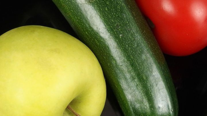 Eine gr&uuml;ne Zucchini liegt neben einem roten Tomaten und einem gr&uuml;nen Apfel auf einem schwarzen Hintergrund, ideal f&uuml;r gesundes Abnehmen.