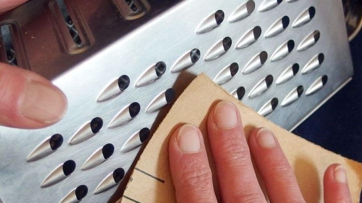 Eine K&uuml;chenreibe wird mit Sandpapier gesch&auml;rft, w&auml;hrend eine Hand das Sandpapier festh&auml;lt und auf die Klingen reibt.