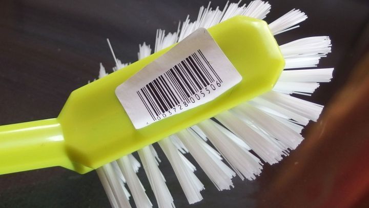 Eine gr&uuml;ne B&uuml;rste mit wei&szlig;en Borsten liegt auf einem Tisch, sichtbar mit einem l&auml;stigen Aufkleber und Barcode.