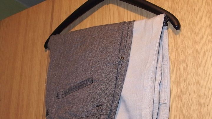 Hosen h&auml;ngen ordentlich auf einem Kleiderb&uuml;gel, vor einem hellen Holzschrank, um sie knitterfrei zu pr&auml;sentieren.
