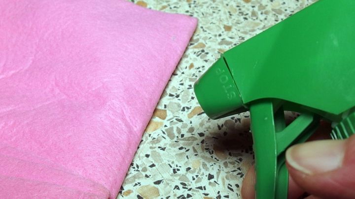 Eine gr&uuml;ne Spr&uuml;hflasche wird gehalten, w&auml;hrend ein pinkes Tuch daneben auf einer marmorierten Oberfl&auml;che liegt.