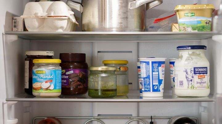 Ein K&uuml;hlschrank zeigt verschiedene Gl&auml;ser mit Lebensmitteln, einem Topf und Joghurt, um Ordnung und Organisation zu verdeutlichen.