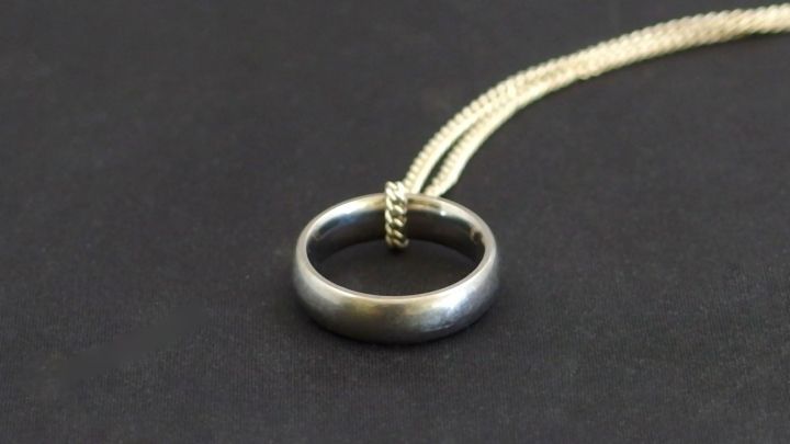 Ein alter Ring h&auml;ngt an einer Kette und wird als Anh&auml;nger getragen, vor einem schwarzen Hintergrund.