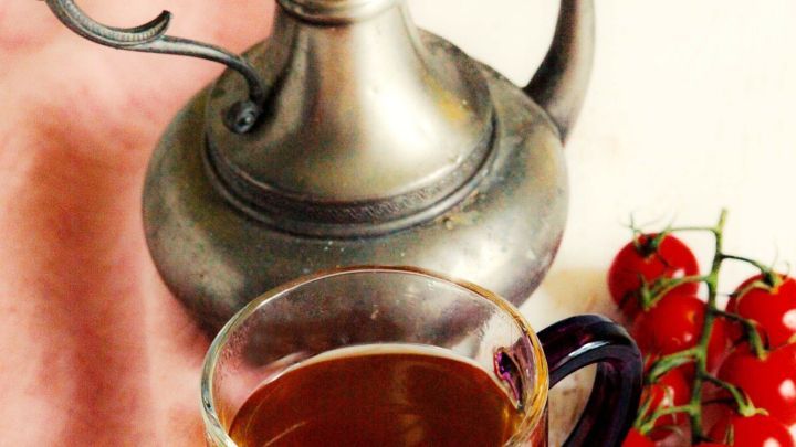 Ein Glas kalter Schwarztee steht neben einer silbernen Kanne und einer kleinen Menge frischer Tomaten auf einem Tuch.