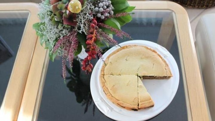 Ein Gedeckter Nusskuchen mit einer Schnittfl&auml;che steht auf einem Tisch neben einer dekorativen Blumenarrangement.