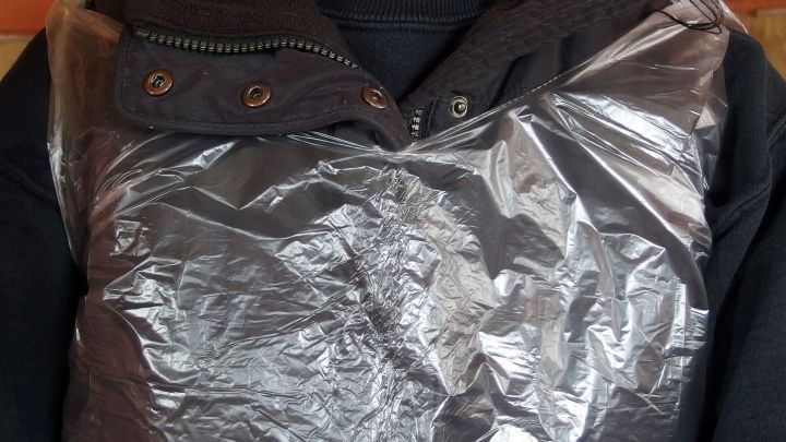 Eine Sch&uuml;rze aus Plastikabfallt&uuml;te mit Griffen wird &uuml;ber einem schwarzen Pullover getragen, praktisch zum Schutz beim Arbeiten.