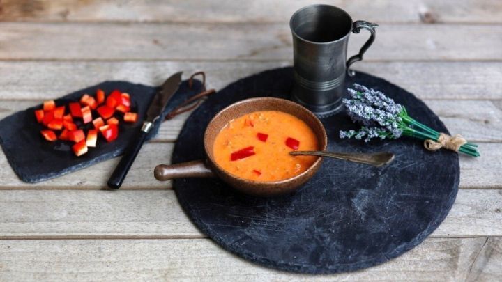 Ein kupferner Topf mit scharfer ungarischer Paprikapaste steht auf einem dunklen Tisch, umgeben von frischen Zutaten.