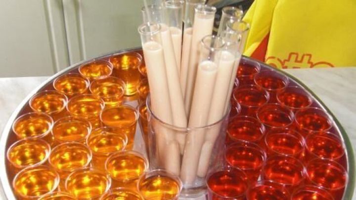 Runde Platte mit buntem Wodka-Wackelpudding in orange und rot, umgeben von langen durchsichtigen Bechern in der Mitte.