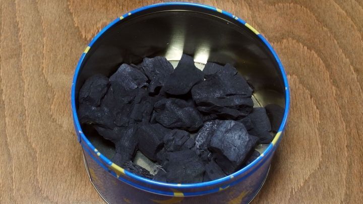 Schwarze Grillkohle liegt in einer runden Metalldose auf einem Holzuntergrund, bereit zur Verwendung in feuchten R&auml;umen.