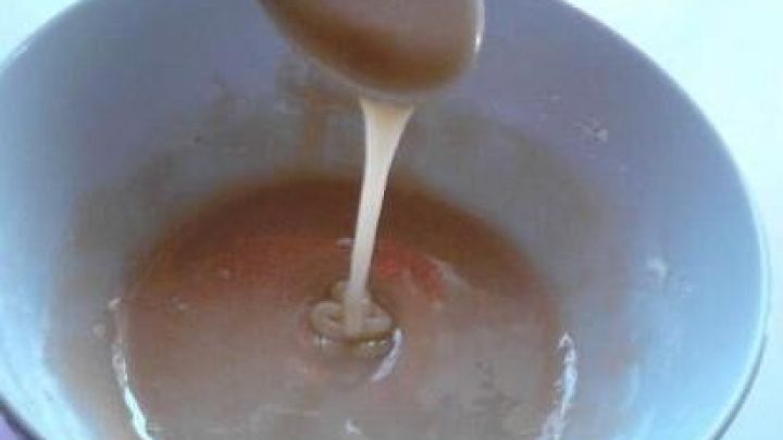 L&ouml;ffel tropft eine cremige Maske aus Honig und Zucker in eine Sch&uuml;ssel, auf einem Tisch stehend.