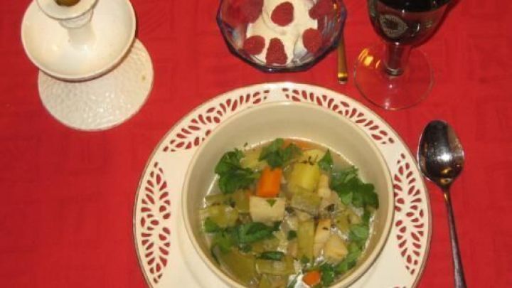 Ein Teller Eintopf mit Gem&uuml;se und Kr&auml;utern steht auf einem dekorativen Tisch mit rotem Tuch, neben Dessert und Rotwein.