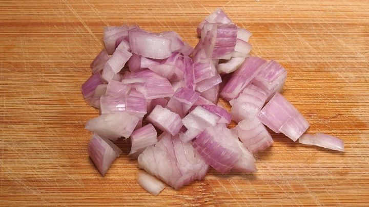 Auf einem Holzbrett liegen frisch gehackte Zwiebeln, die f&uuml;r das Kochen vorbereitet sind und einen intensiven Duft verbreiten.