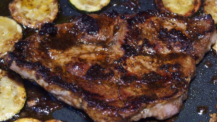 Ein saftiges St&uuml;ck Fleisch brutzelt in einer Pfanne, umgeben von goldbraun gebratenen Zucchinischeiben.