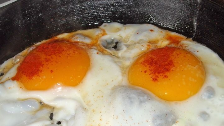 In einer Gusseisenpfanne braten zwei Spiegeleier mit leuchtend orangefarbenen Eigelben in einer hei&szlig;en Umgebung.