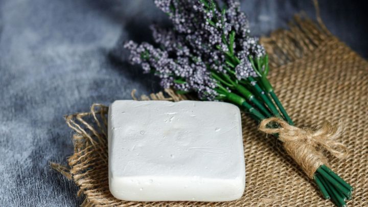 Eine zarte Ziegenmilchseife liegt auf einem Jutesack, umgeben von einem Bund Lavendel in sanfter Beleuchtung.