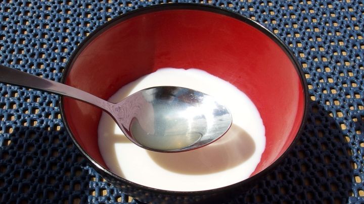 In einer roten Sch&uuml;ssel befindet sich Cr&egrave;me fra&icirc;che, w&auml;hrend ein L&ouml;ffel darin liegt, auf einem blauen Tisch.