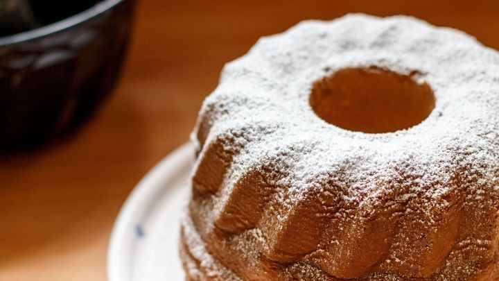 Ein Gugelhupf mit Puderzuckerbestreuung steht auf einem Teller in einer warmen, einladenden K&uuml;chenumgebung.