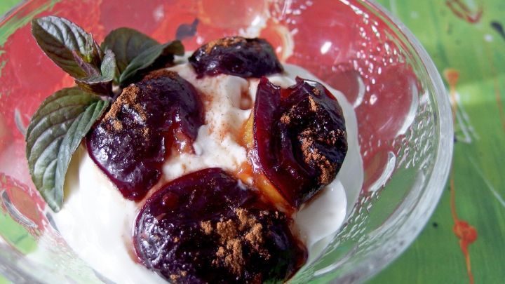 Karamellisierte Pflaumen liegen auf einer cremigen Vanille-Quarkcreme in einer Sch&uuml;ssel, umgeben von einem bunten Hintergrund.