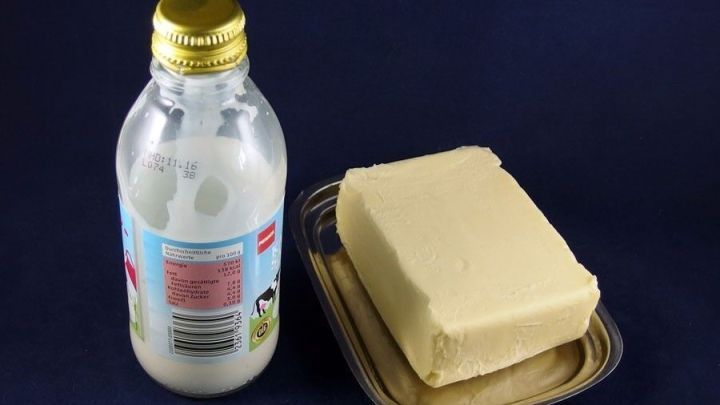Eine Flasche Kondensmilch steht neben einem St&uuml;ck Butter auf einem goldenen Teller, alles vor einem dunkelblauen Hintergrund.