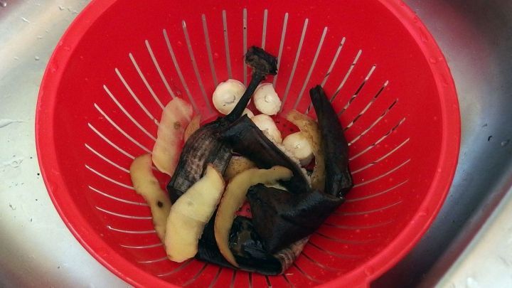 Rotes Sieb im K&uuml;chensp&uuml;lbecken enth&auml;lt Abf&auml;lle wie Obstschalen. Umgebung: Edelstahlsp&uuml;le mit Wassertropfen.