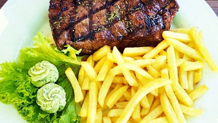 Ein saftiges Steak liegt auf einem Teller, umgeben von knusprigen Pommes und frischem Salat mit Kr&auml;uterbutter.