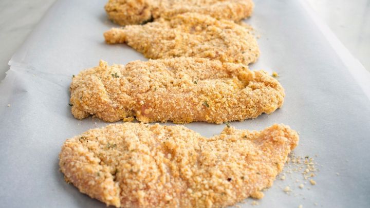 Panierte Schweineschnitzel liegen auf Backpapier und warten darauf, im Backofen gebacken zu werden.