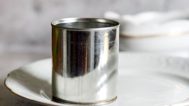 Ein gl&auml;nzender Dosenring steht auf einem wei&szlig;en Teller, umgeben von einer rustikalen K&uuml;chentextur im Hintergrund.