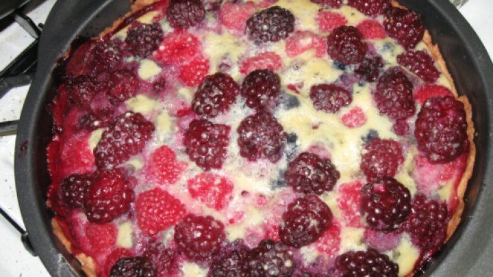 Eine Mixed Berry Pie mit knusprigem Krustenrand gef&uuml;llt mit leuchtenden Beeren backt im Ofen in einer runden schwarzen Form.